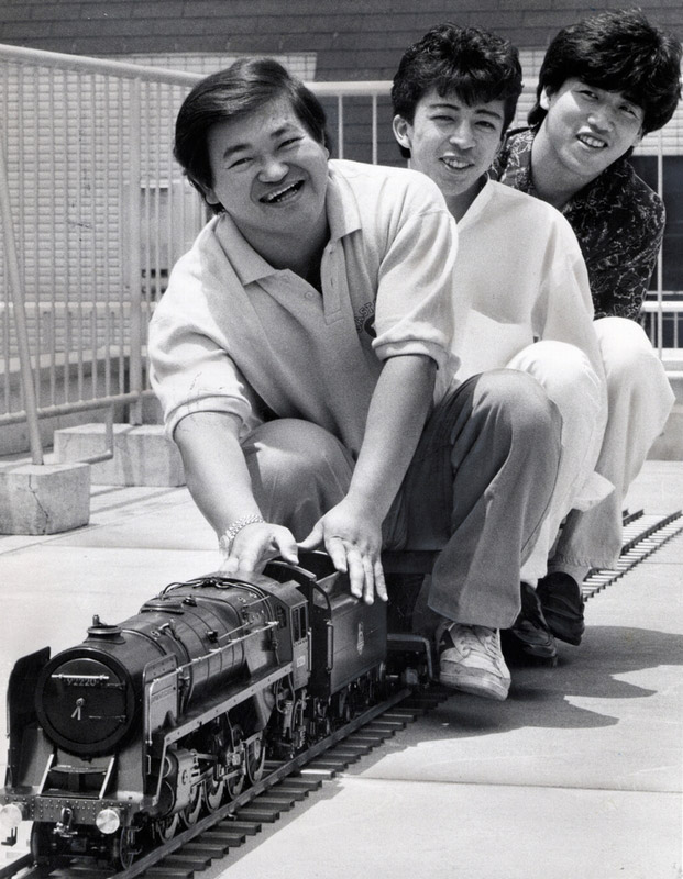 ハドソン社員と模型機関車に乗って楽しむ高橋名人（手前）＝1987年6月28日