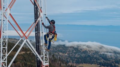 T-Mobile worker climbing tall microwave tower with mountain in background
