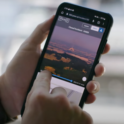 A person’s hand holds a smart phone while their other hand taps a video of a landscape.