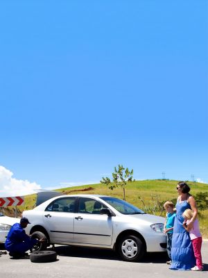 A family standing next to their car as a AAA employee changes their tire