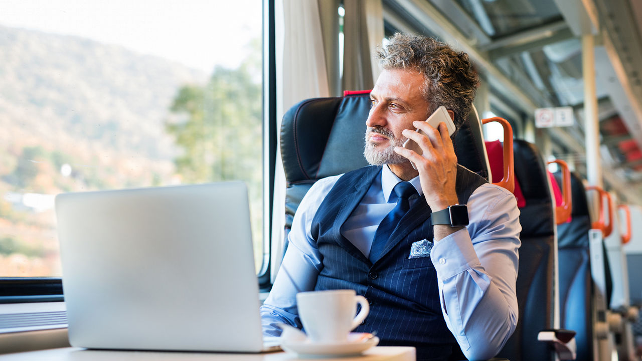Man sitting in train working on his laptop and taking a call