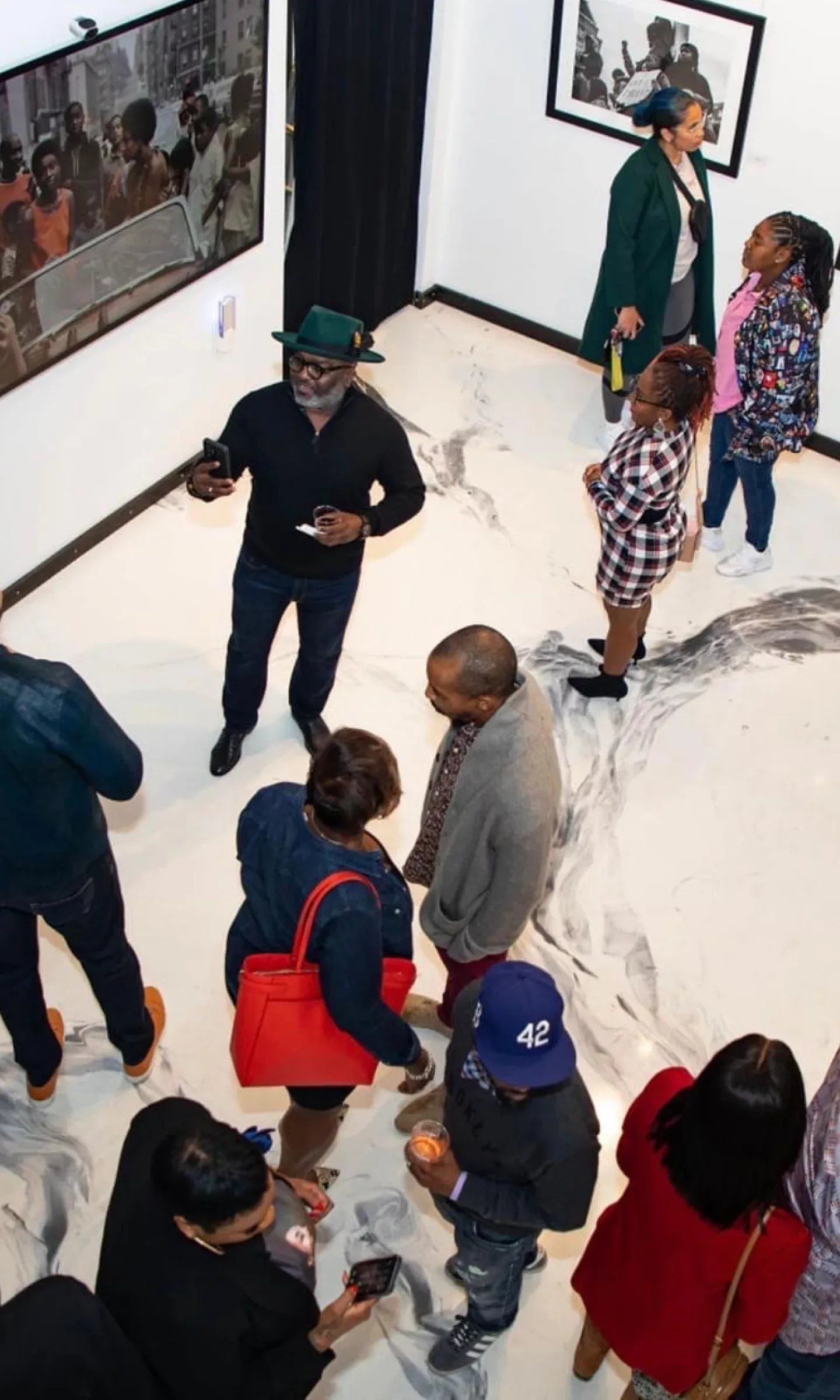 Bird’s-eye view of a group of people standing in an art gallery with framed art hanging on white walls
