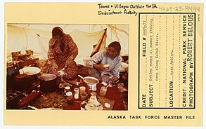 Alaskan park services slip showing two women preparing and storing fish at a summer fishing camp along the Kobuk river. They have many pots and jars out on a table to prepare their fish.