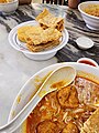 Image 64A bowl of curry mee, with fried beancurd skins and fish cake on the side (from Malaysian cuisine)