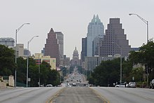 Photograph of the Texas Capitol dome framed between tall buildings along a street