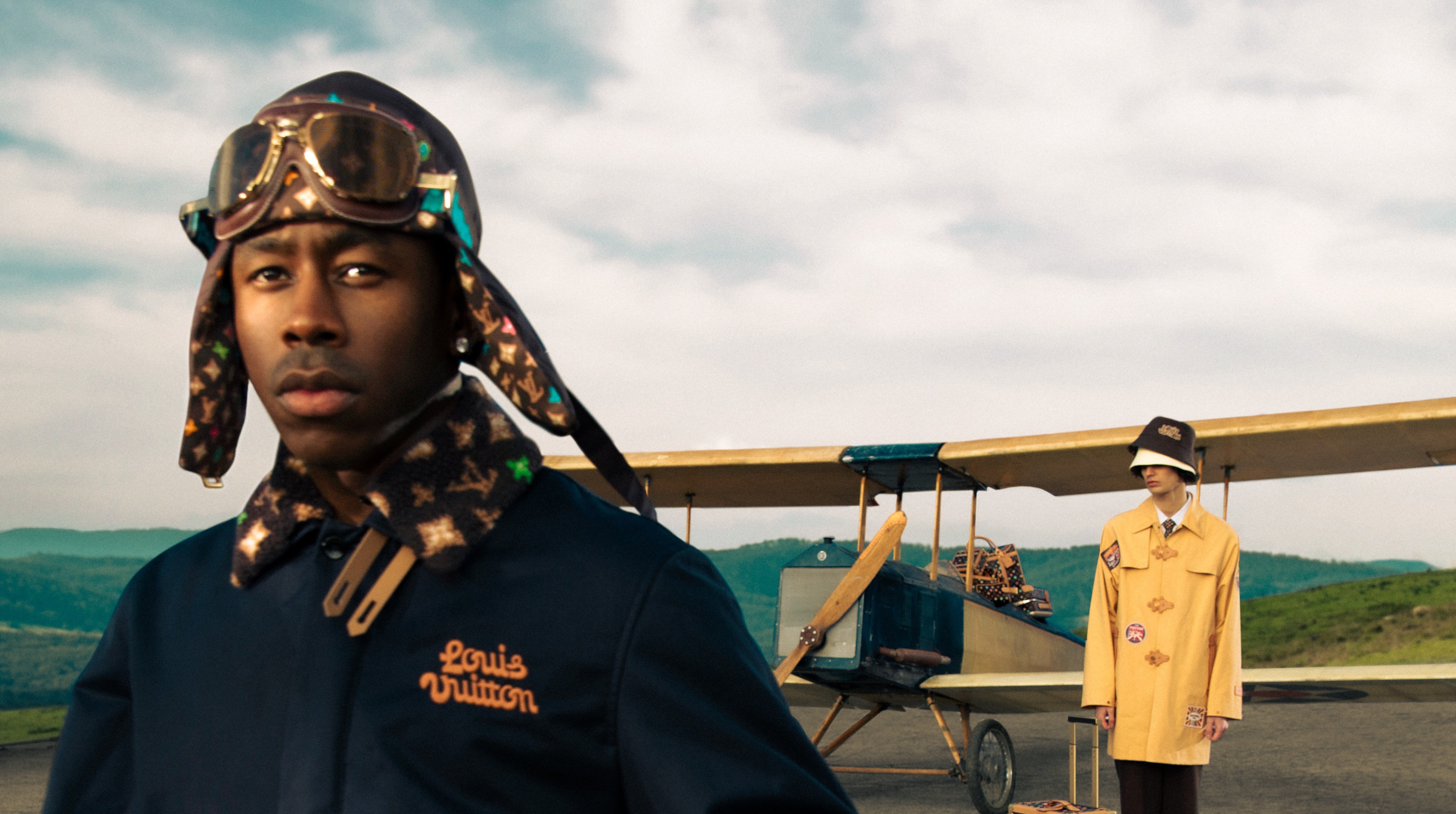 Tyler, the Creator poses in front of a vintage airplane in a look from his spring 2024 men's capsule collection for Louis Vuitton.
