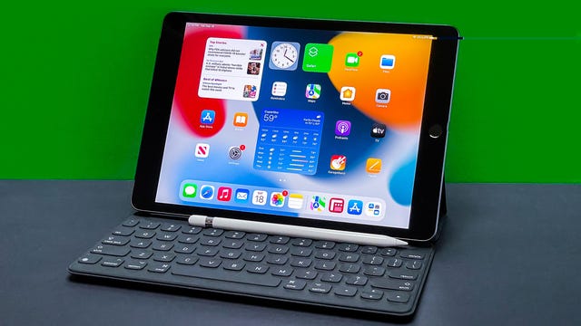 9th Gen iPad with accessories sits on gray surface with green background.