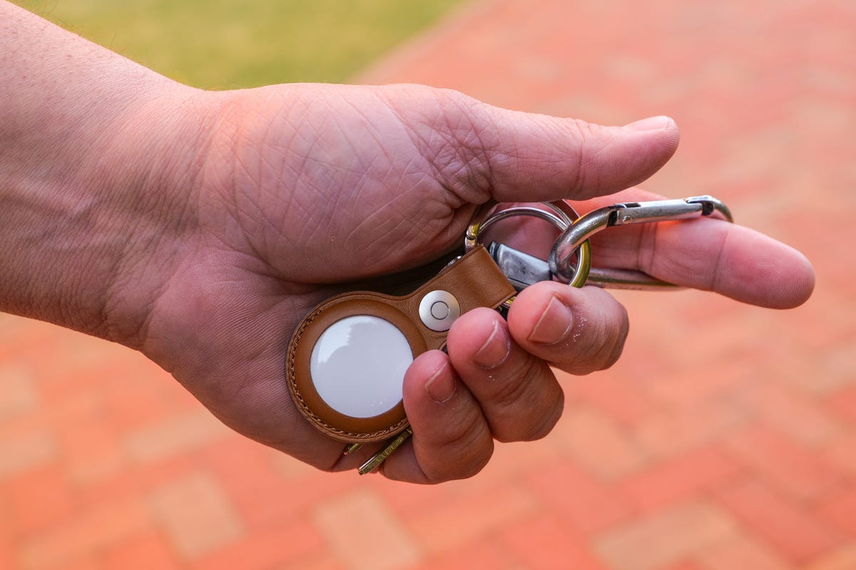 A hand holding an AirTag in a keyring accessory