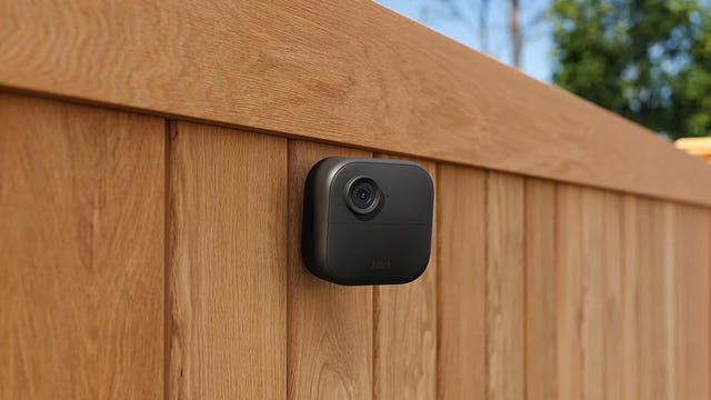 A Blink outdoor camera mounted to a wooden fence in a backyard.