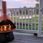 An orange Chiminea with three flames in front of a sunset over a golf course