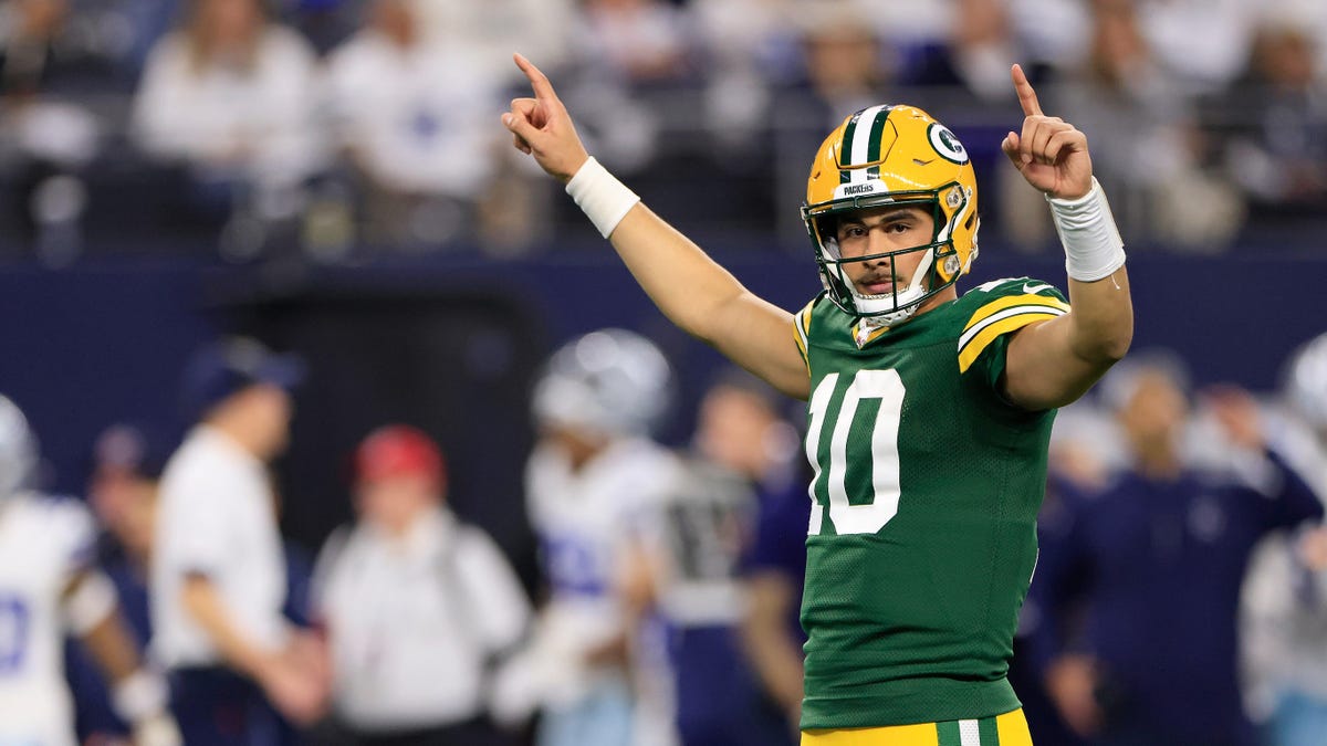 Jordan Love of the Green Bay Packers celebrating a touchdown posting with arms aloft, both index fingers pointing upward.