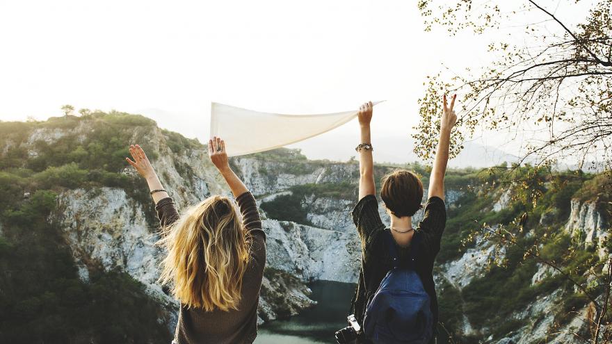 Dos chicas de espaldas levantando un pañuelo en paisaje de montaña