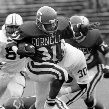 A Cornell football player runs with the ball in between defensemen.