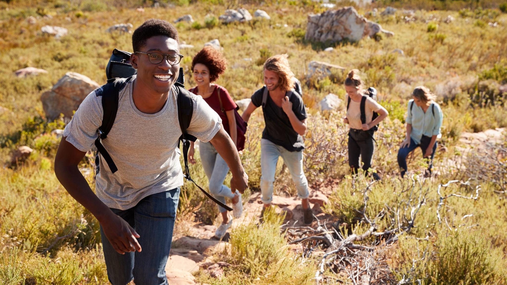 A smiling black man leads a group of friends up a trail.