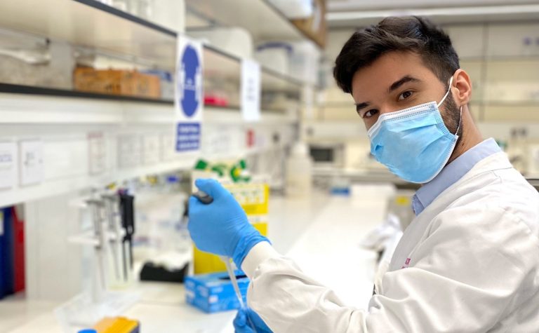 Researcher wearing mask and white lab coat holding pipette