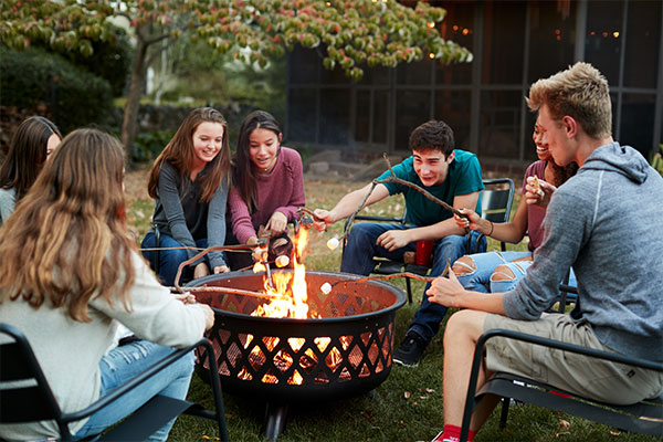 A group of teenagers roasting mashmellows over a fire pit
