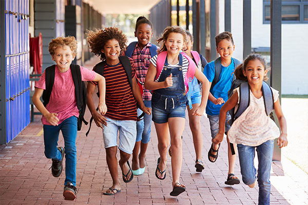 A group of elementary students running down an outdoor hallway