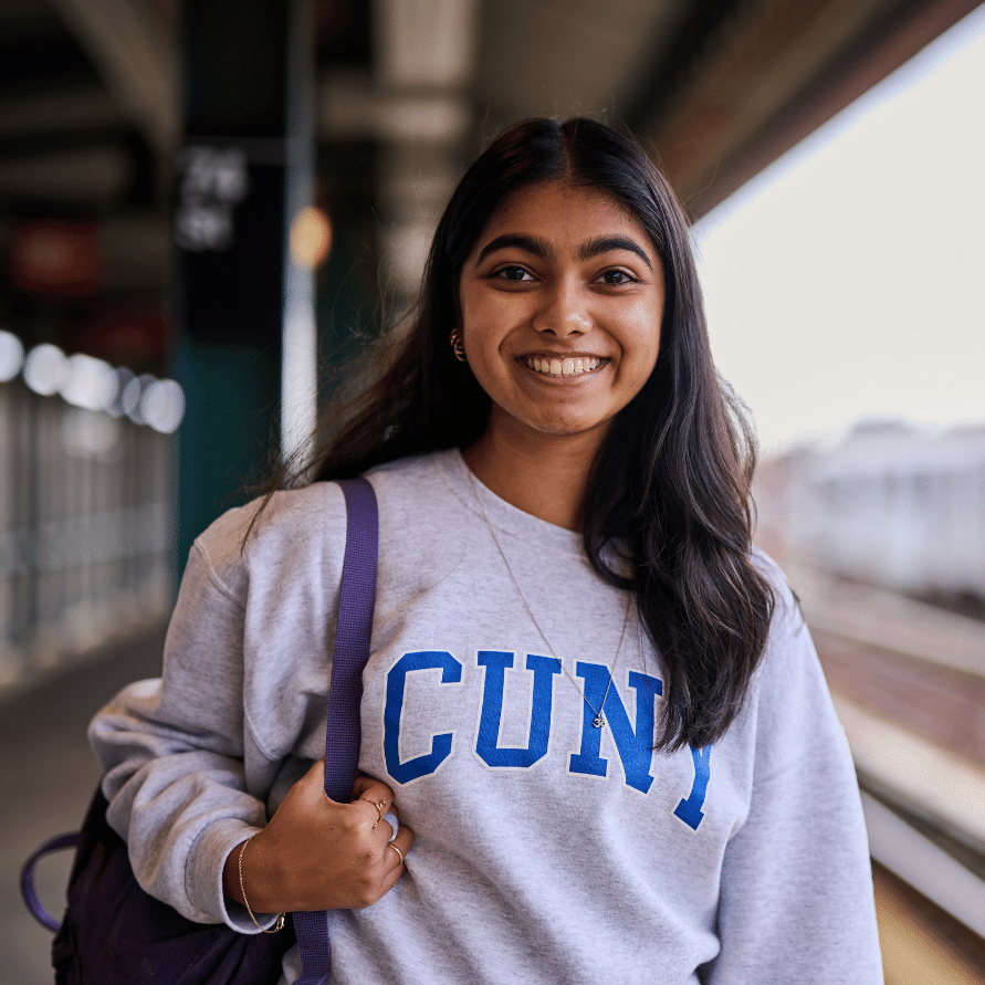A CUNY student smiling on an elevated subway platform.