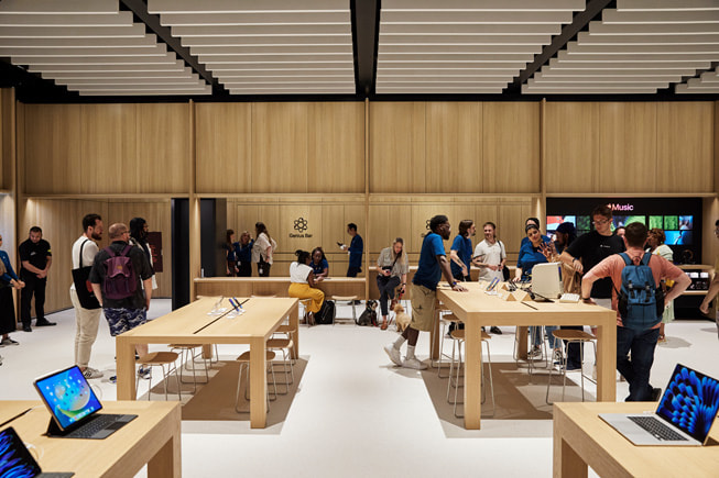 Zdjęcie wnętrza jednego z salonów Apple Store i znajdujących się w nim klientów i pracowników.