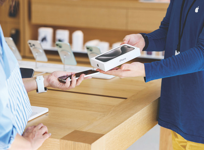 Imagem representando o programa Apple Trade In mostra uma cliente trocando um iPhone antigo por um aparelho novo na caixa.