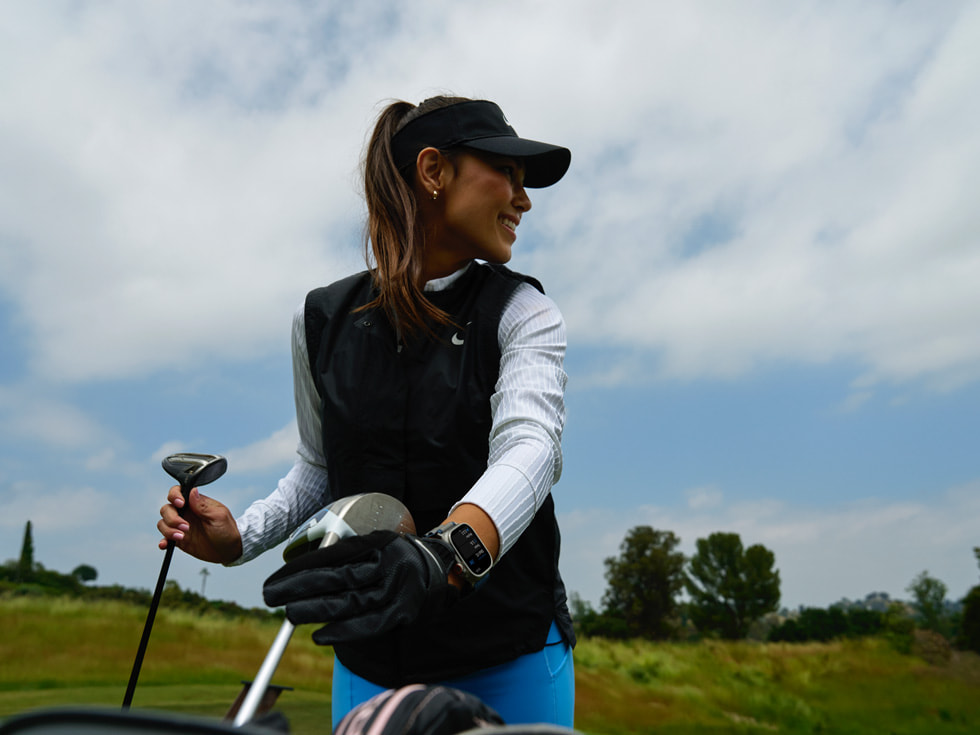 Une golfeuse portant une Apple Watch tient deux clubs de golf.