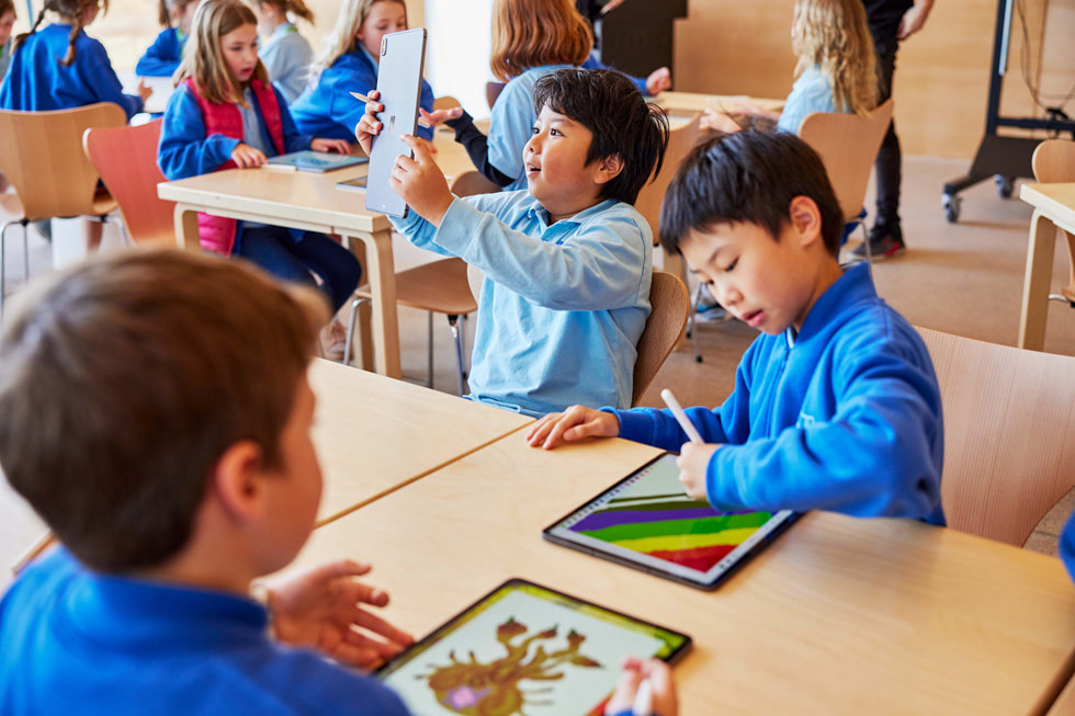Młodzi uczniowie przy stole używający iPada Pro i Apple Pencil.