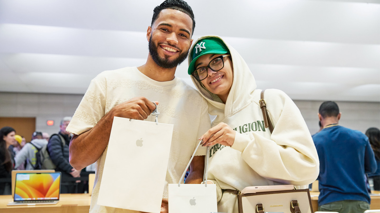 Twee klanten houden tassen met hun nieuwe aankopen omhoog in Apple Fifth Avenue in New York.