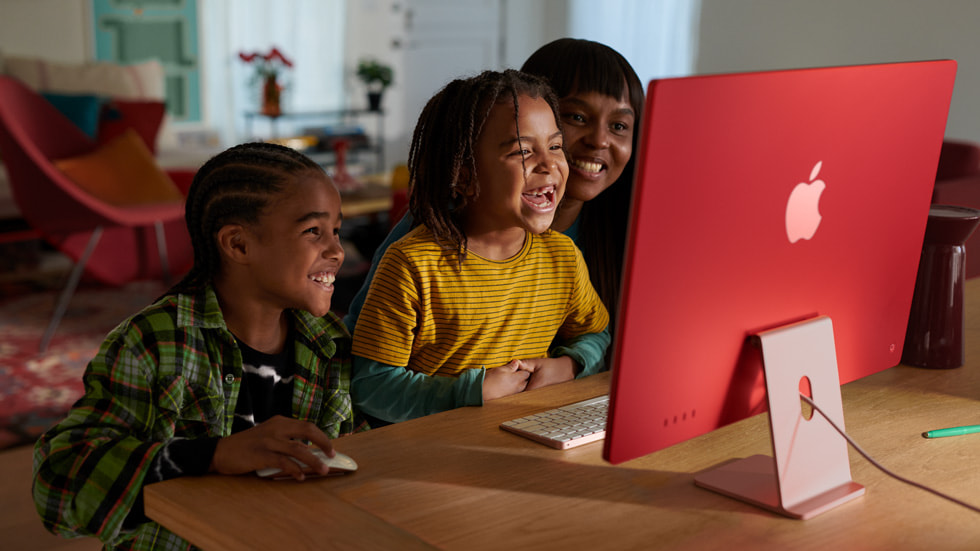 Tres integrantes de una familia miran la nueva iMac con chip M3 en rosa, con teclado y mouse del mismo color.