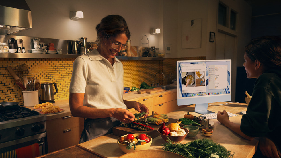 A parent and their child are shown cooking in a kitchen and using the new iMac with M3 in blue and color-matched keyboard and mouse.