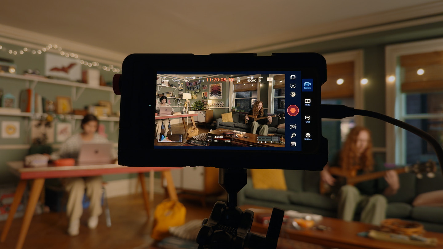 En iPhone 15 Pro Max på en kamerarigg brukes til å filme en person som sitter ved et skrivebord og jobber på en MacBook.