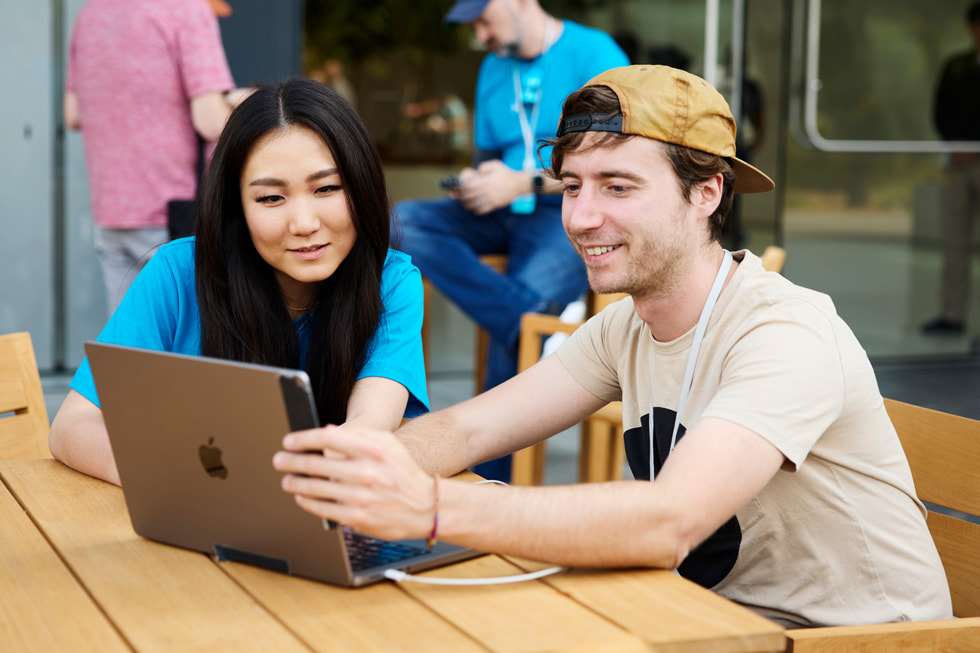 Two people look at a MacBook during WWDC23’s Meet the Developers event.