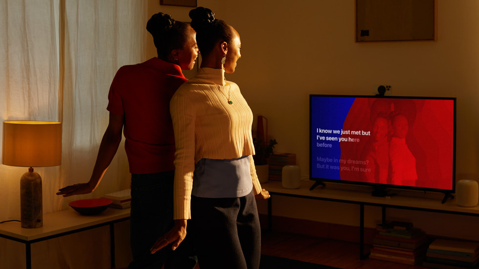 Två Apple-användare poserar med ryggarna mot varandra och speglas på tv-skärmen.