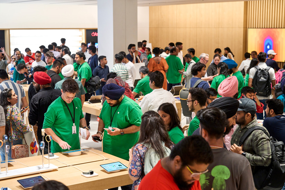 Apple Saket 店內，顧客與 Apple 團隊成員交談並圍繞在展示桌旁探索店內眾多裝置。