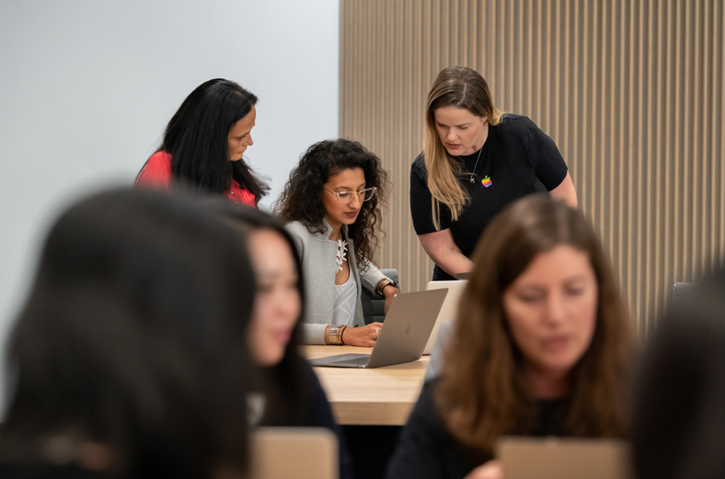 Derrière un MacBook, des femmes travaillent avec deux instructrices. 