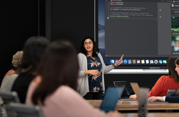 Une instructrice montre du code sur MacBook Pro à une classe de participantes. 