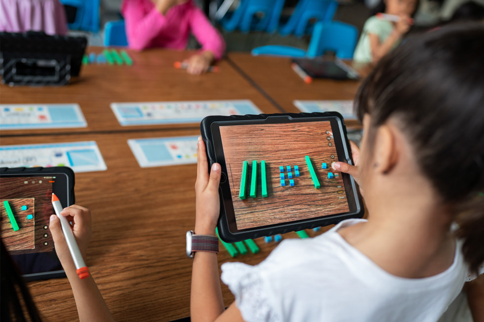 Uma aluna é mostrada usando o iPad em um ambiente de sala de aula.