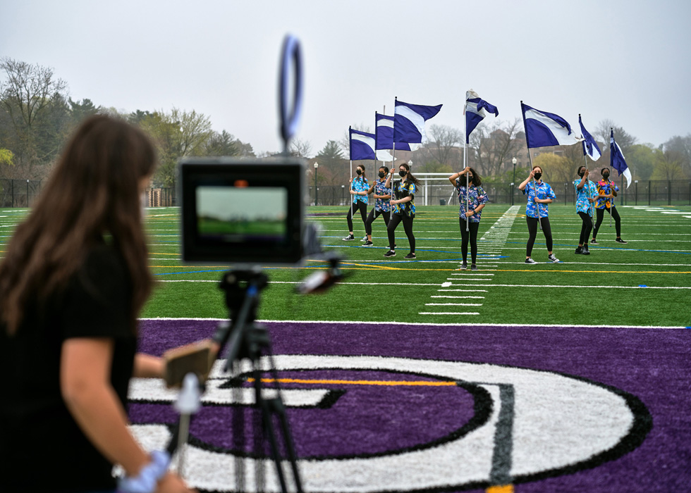 Een leerling van New Rochelle High School gebruikt een iPad om leerlingen te filmen die met vlaggen op het sportveld lopen.