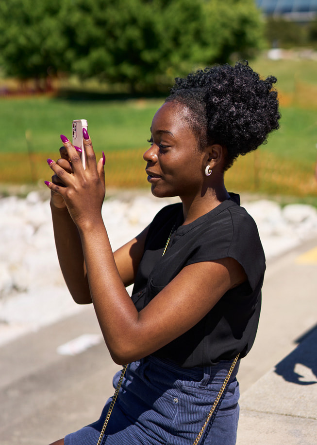 Adetokunbo Opeifa hält ihr iPhone hoch, um ein Foto in einem Park zu machen.

