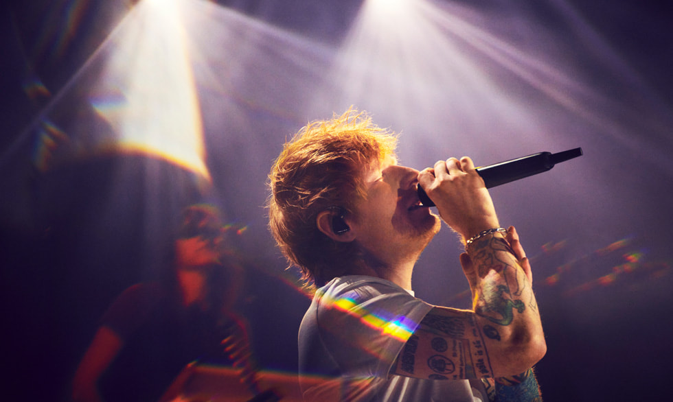 Singer-songwriter Ed Sheeran staat op een podium te zingen met een microfoon.