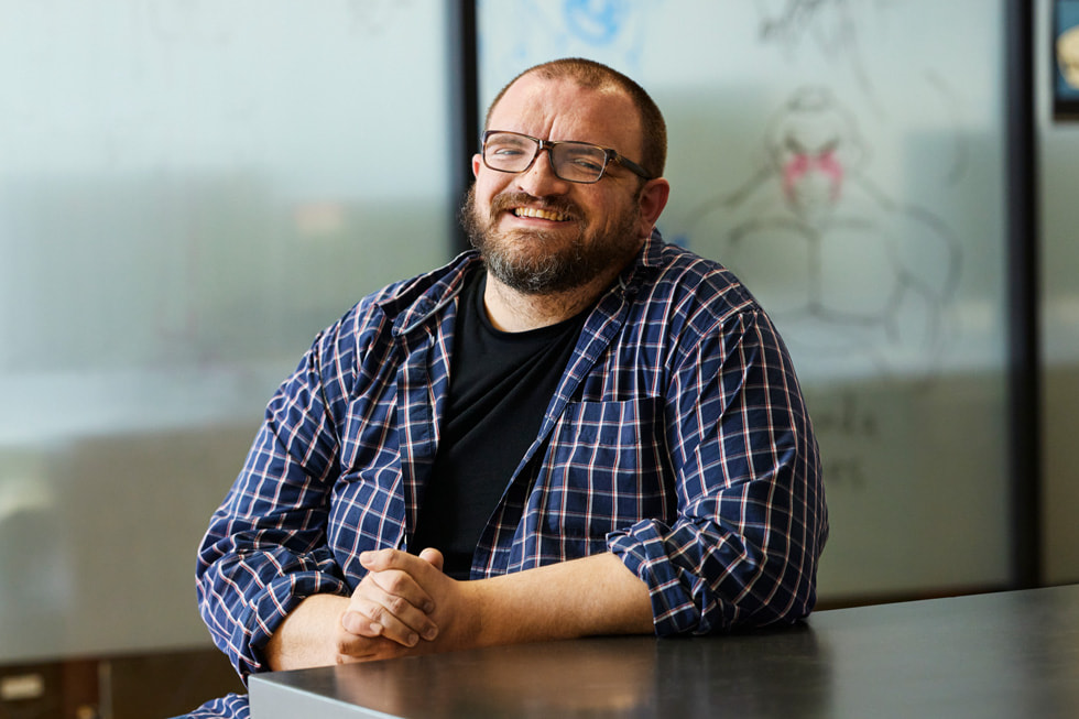 A portrait of academic dean Tim Dailey. Dailey is seated at a table and wearing a plaid button-down over a black T-shirt and a pair of glasses.