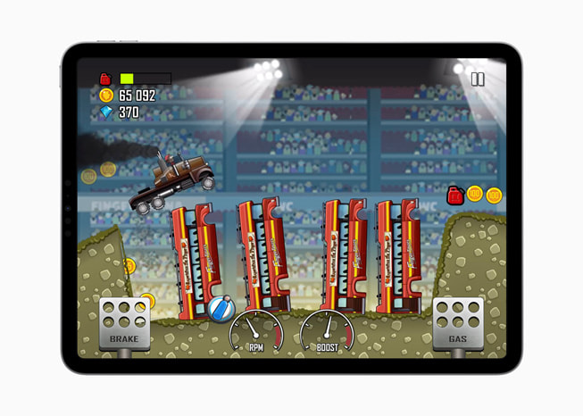 Klatka z gry Hill Climb Racing+ na iPadzie Pro pokazująca monster trucka skaczącego przez wyrwę, w której stoją wozy straży pożarnej.