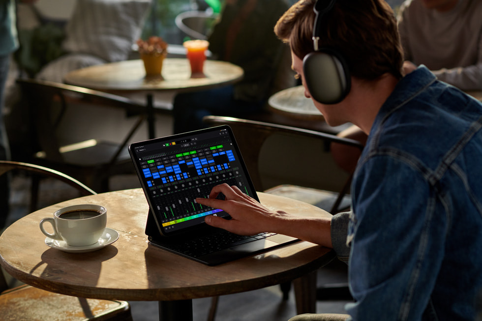 A person wearing headphones sits at a table with coffee using Logic Pro for iPad.
