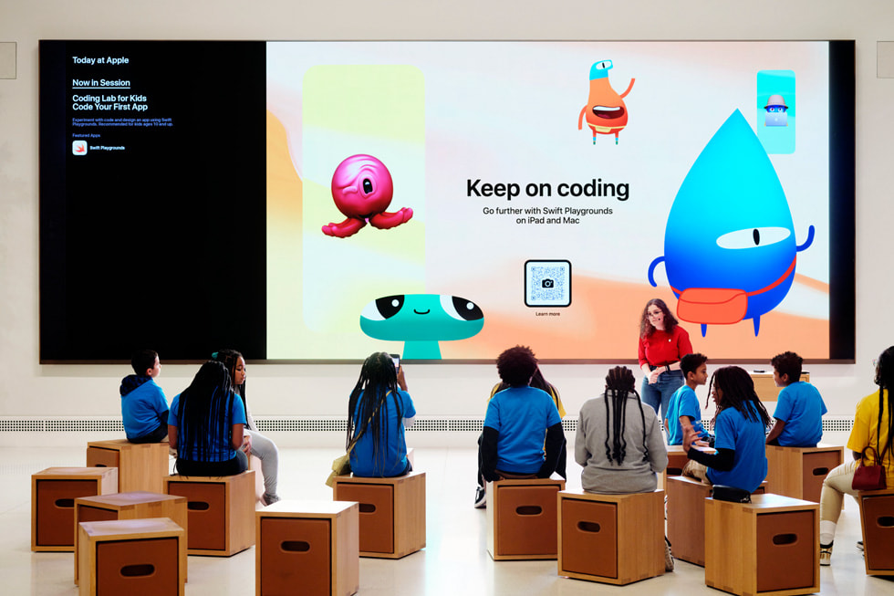 Students sit in a Forum at an Apple Store for a Today at Apple session titled Coding Lab for Kids: Code Your First App.