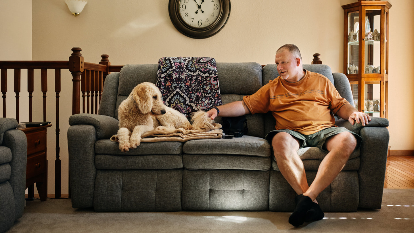 Robert Guithues est assis sur son canapé chez lui avec son chien.