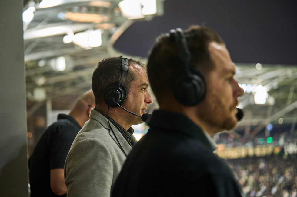 Os locutores e comentaristas Max Bretos e Brian Dunseth são mostrados usando fones de ouvido nos bastidores de uma partida do LAFC.