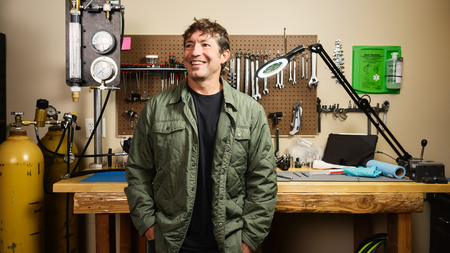 Mike Huish, CEO of Huish Outdoors, stands in front of a work bench with an array of tools and scuba gear. 