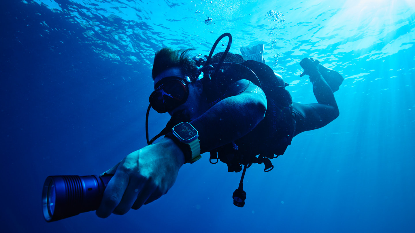 A scuba diver wearing Apple Watch Ultra with Oceanic+ swims under the ocean’s surface.