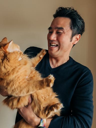 Fotoportrett av Tetsu, som smiler og ser på katten sin, som han holder.