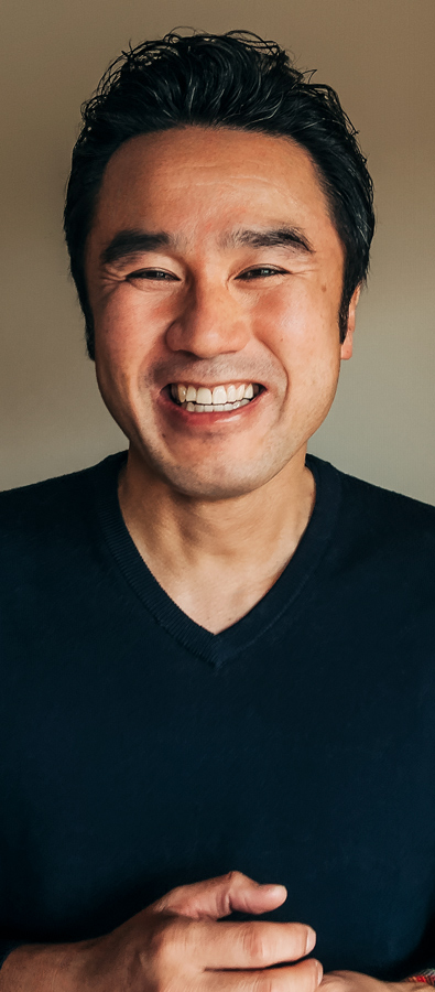 Portretowe zdjęcie Tetsu, który szeroko się uśmiecha i kieruje wzrok w stronę czytających.