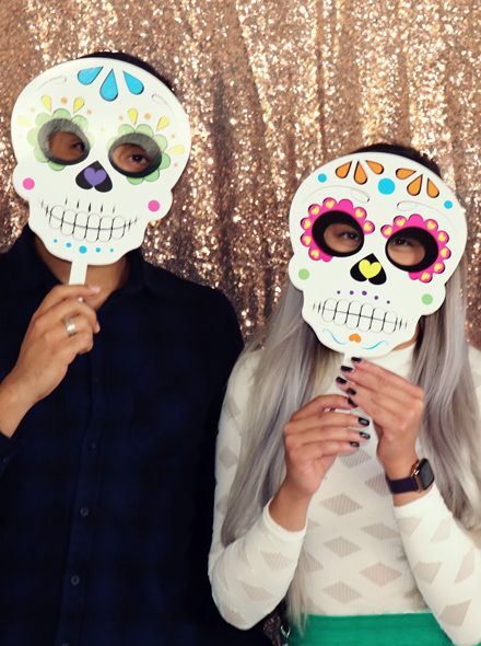 Foto von zwei Personen, die Masken vom mexikanischen Tag der Toten vor ihre Gesichter halten.